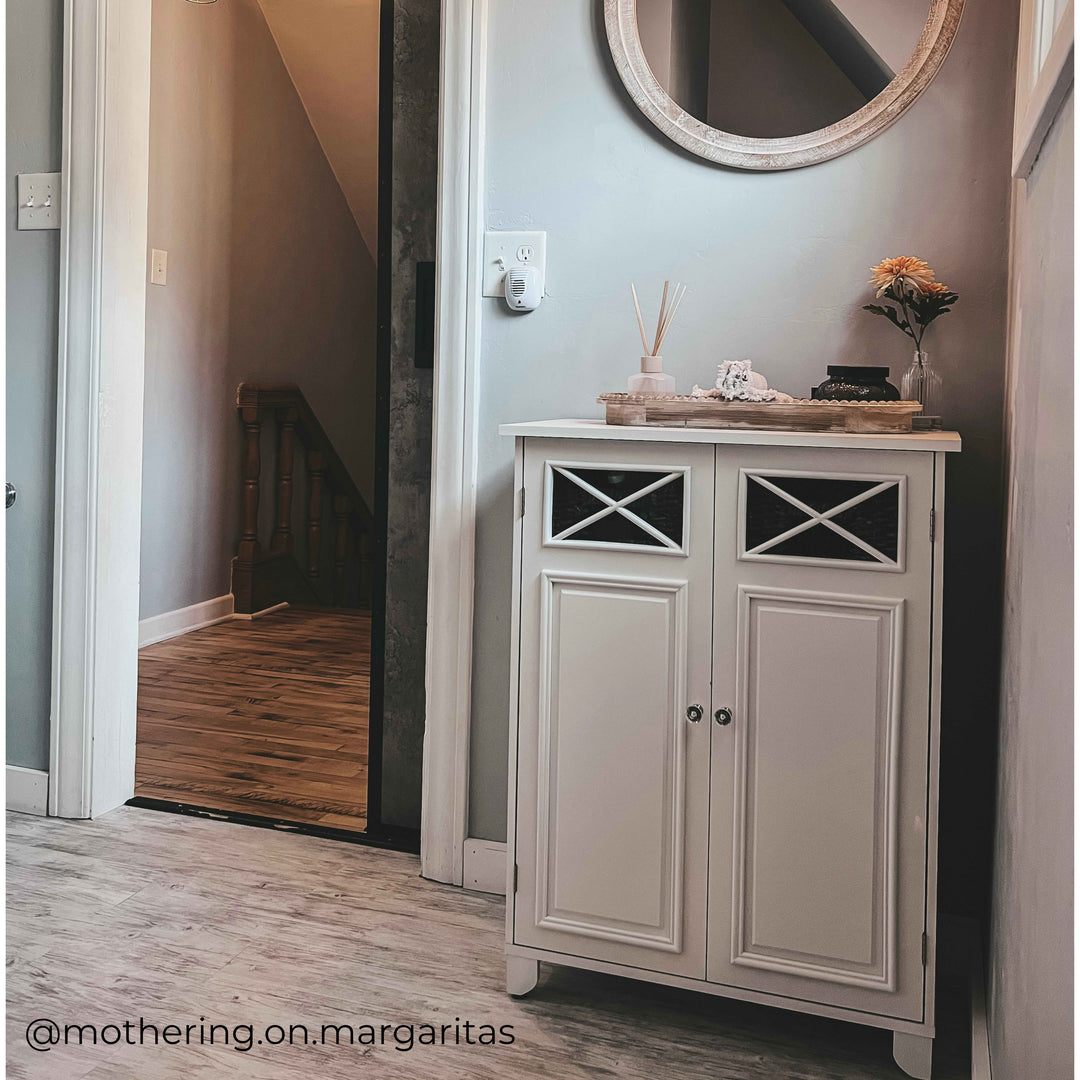 White floor cabinet with decor items ontop in an entryway. 