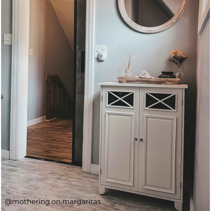 White floor cabinet with decor items ontop in an entryway. 