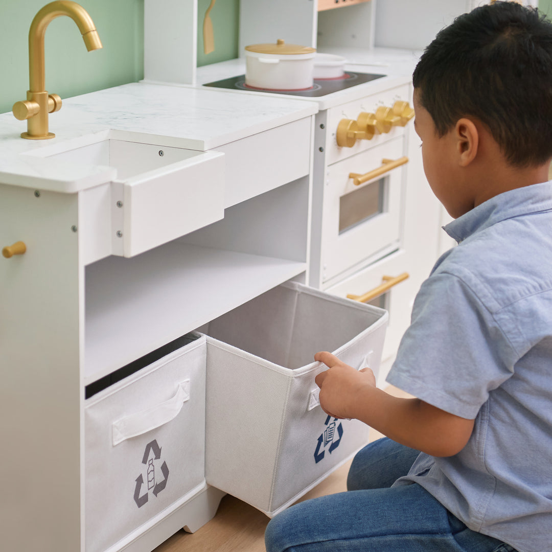 Boy opening a TEAMSON KIDS - LITTLE CHEF ATLANTA LARGE MODULAR PLAY KITCHEN, WHITE/GOLD drawer in a modern kitchen.
