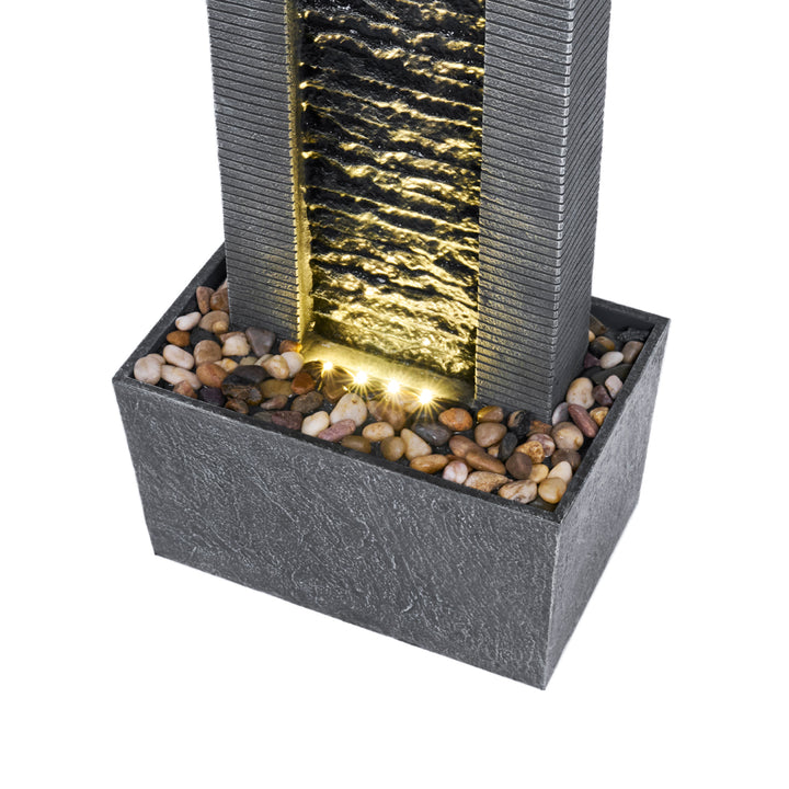 A close-up of the base of the fountain, featuring the LED light and pebbled surface