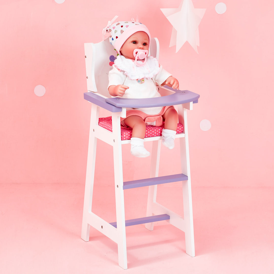 A baby doll sitting inside a highchair for dolls, white with pink cushion and purple tray